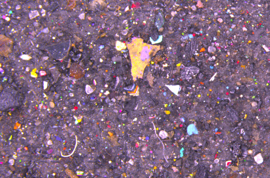 Microscopia mostra microplásticos coloridos e, ao centro, fragmento da parede com camadas de grafite